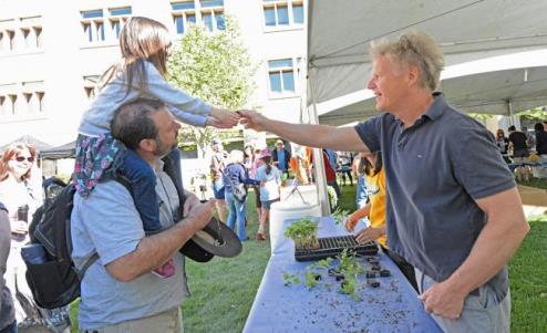 Plant Sciences professor John Yoder, right, hands a Shady Lady tomato seedling to 4-year-old Evie Kraushaar, on her father James' shoulders. (photo: Cody Kitaura/UC Davis)