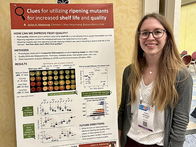 A young woman standing by a research poster and smiling