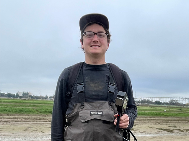 A man in a broad, open place holding a gizmo. Sky is cloudy-gray