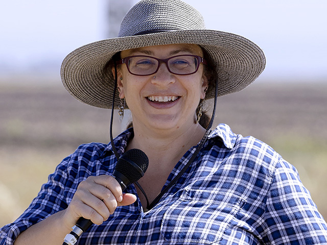 Close-up of a woman wearing a broad-brimmed hat, smiling big and holding a microphone