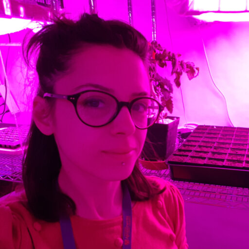 Woman standing in front of greenhouse plants. Pink lighting