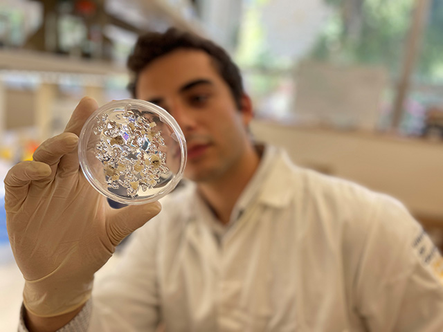 Man in white lab coat holding a glass dish in a gloved hand.