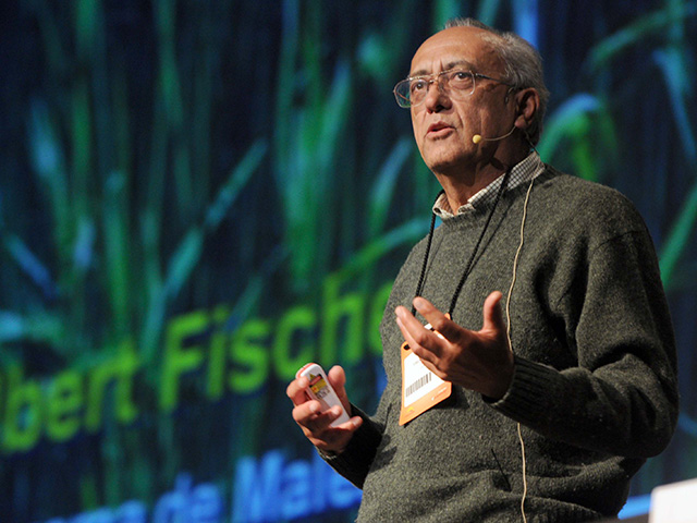 Man speaking at an indoor venue, with the name "Albert Fischer" in the background.