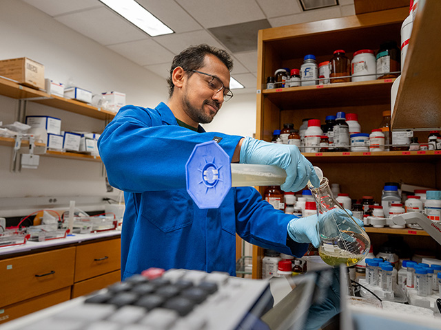 Man in a lab pouring something from one container into another
