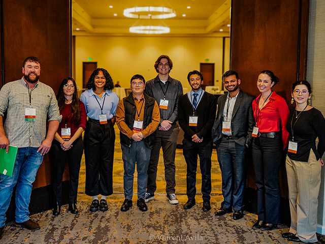A man stands with a group of eight professionally dressed young people, standing together in a conference setting, smiling. UC Davis Department of Plant Sciences