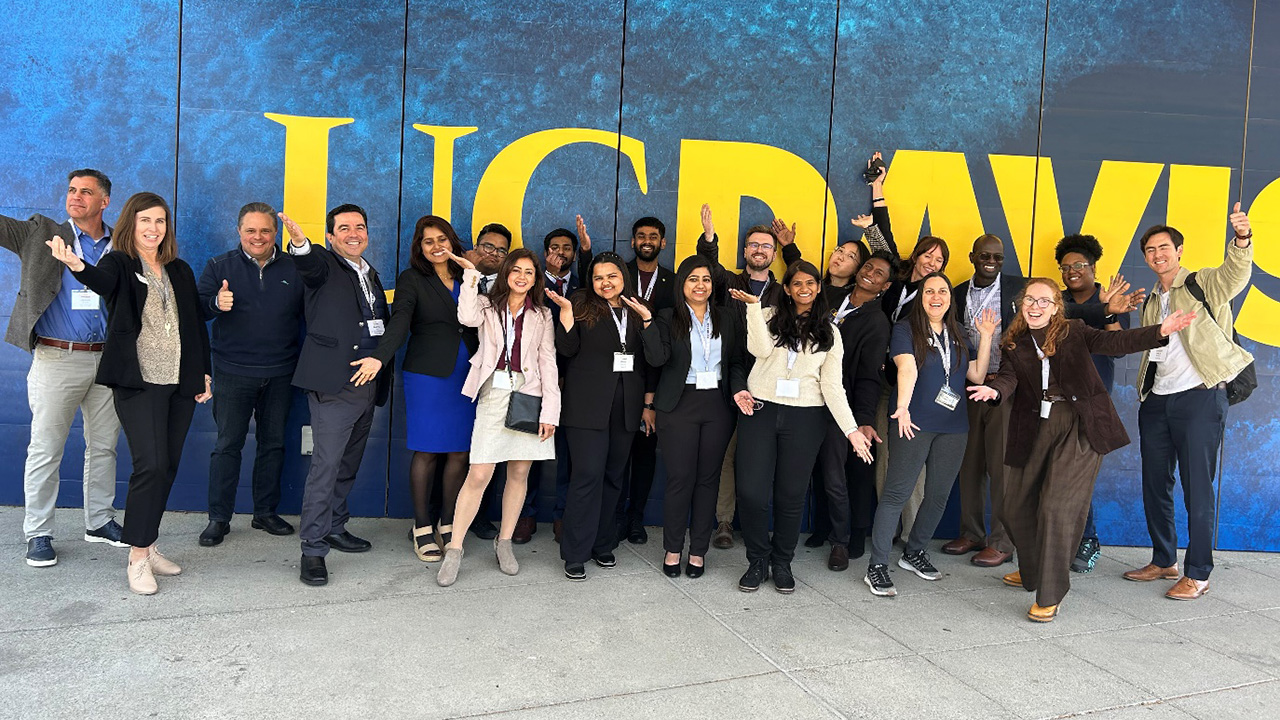 A large group of young people, all dressed professionally, lined up in front of a giant sign that says "UC Davis"