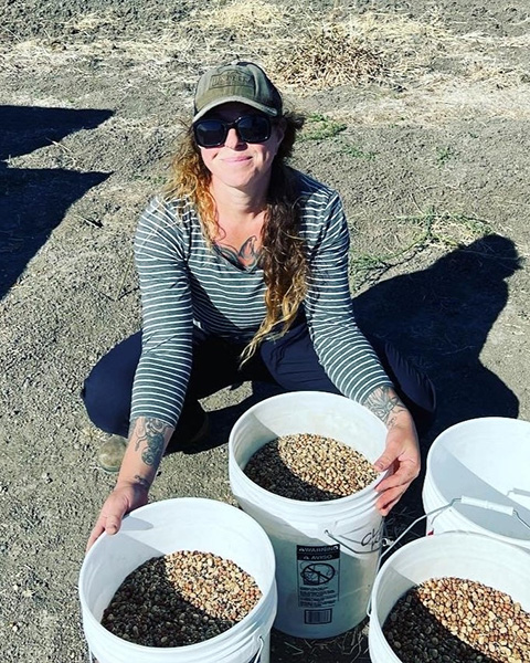 Woman squatting on the ground, with large buckets of pinto beans