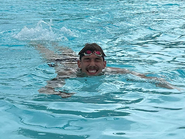 Smiling swimmer in black cap and red goggles -- his eyes scrunched up comically -- splashes through blue pool.. UC Davis Department of Plant Sciences