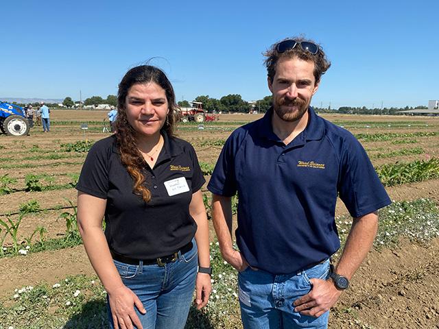 A woman and a man, standing in front of a field. Blue sky above.
