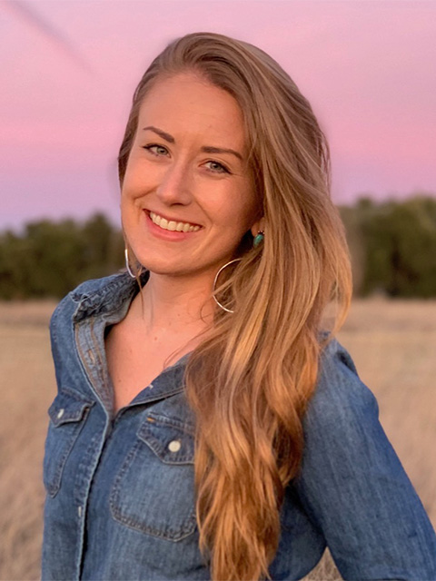 A woman with long blonde hair, smiling, a pink sunset sky in the background