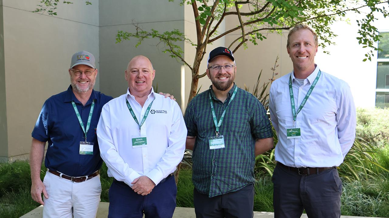 Four men wearing lanyards standing outdoors by shrubs, smiling. UC Davis Department of Plant Sciences