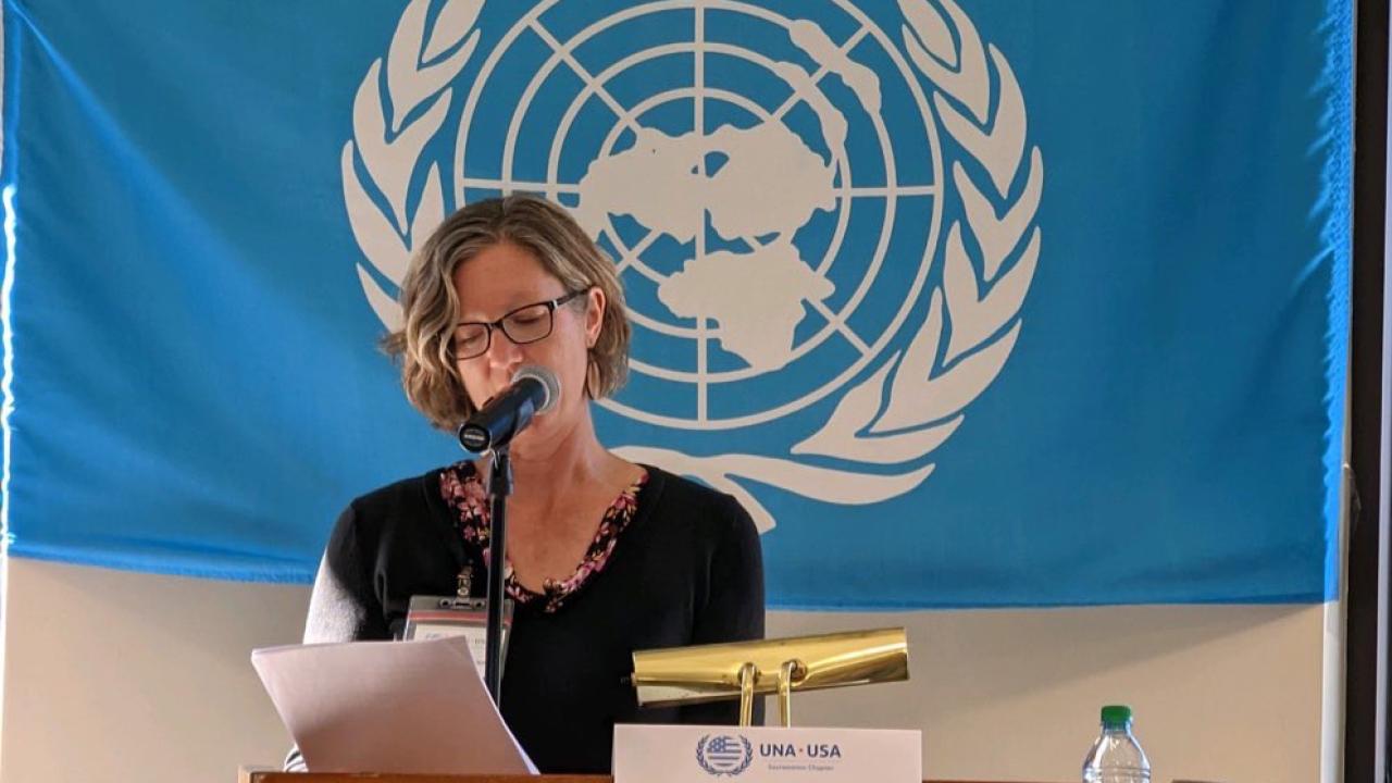 Woman speaking at a podium with the United Nations symbol behind  yher