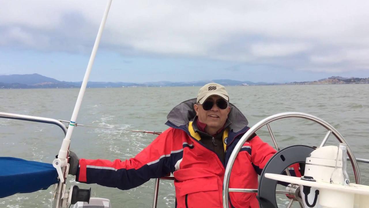 Man wearing a bright orange jacket in a boat, with water, hills and clouds in the background