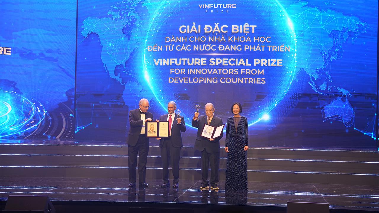 Four people on a stage, dressed in formal wear, with bright blue lights behind them.