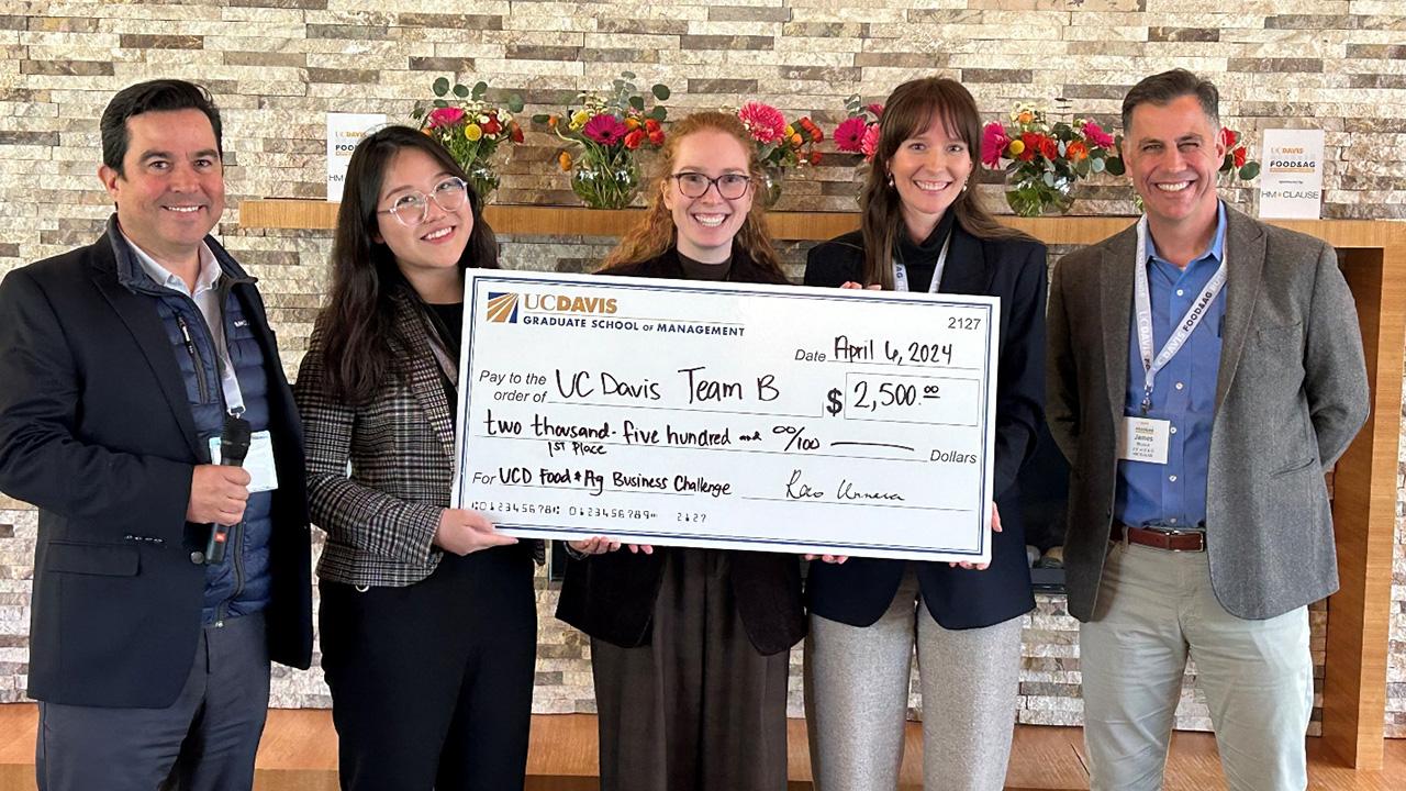 Three women hold a giant check and smile. The check is for 2,500 dollars.Two men flank them.