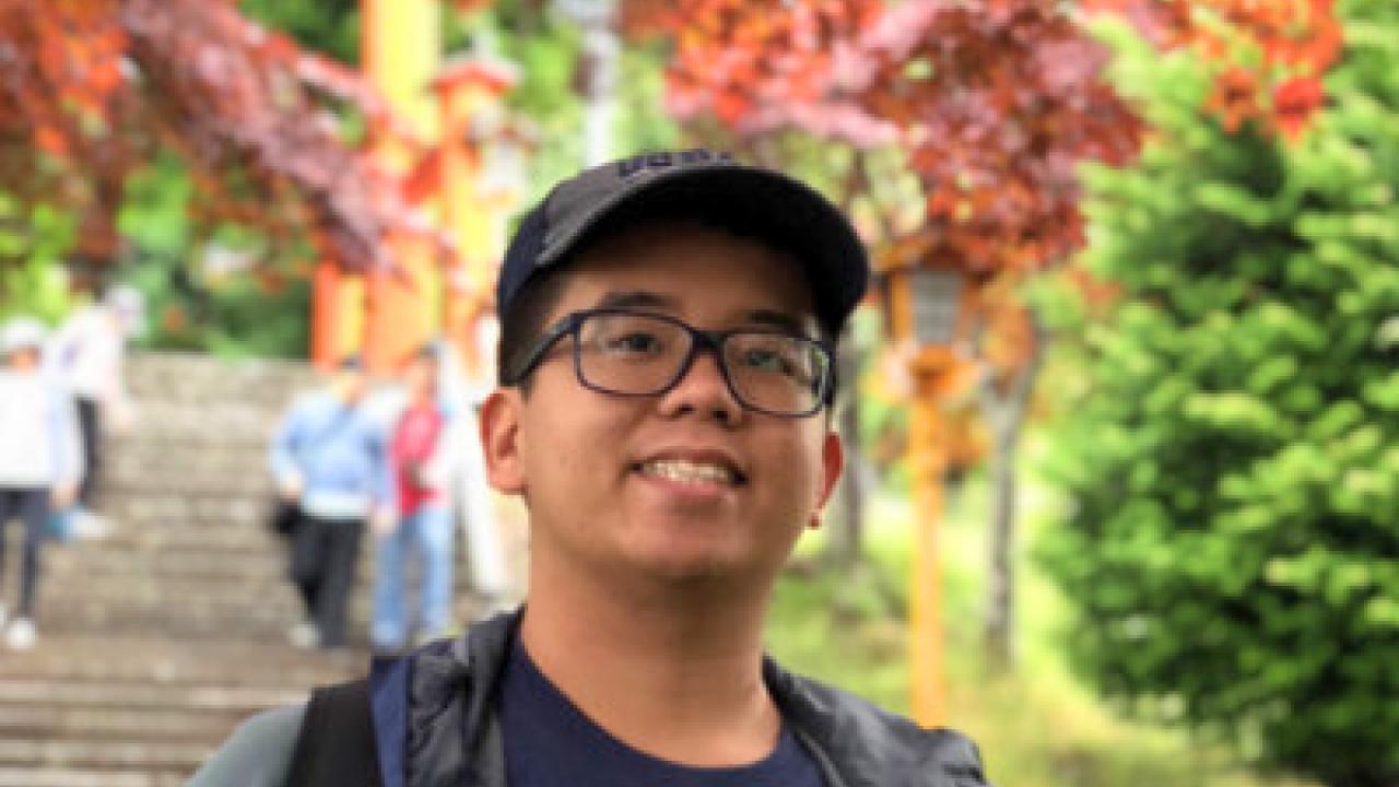 Asian man smiles in front of tree with red leaves 