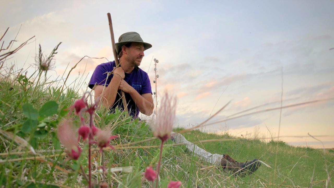 Man sits in peaceful field holding walking stick