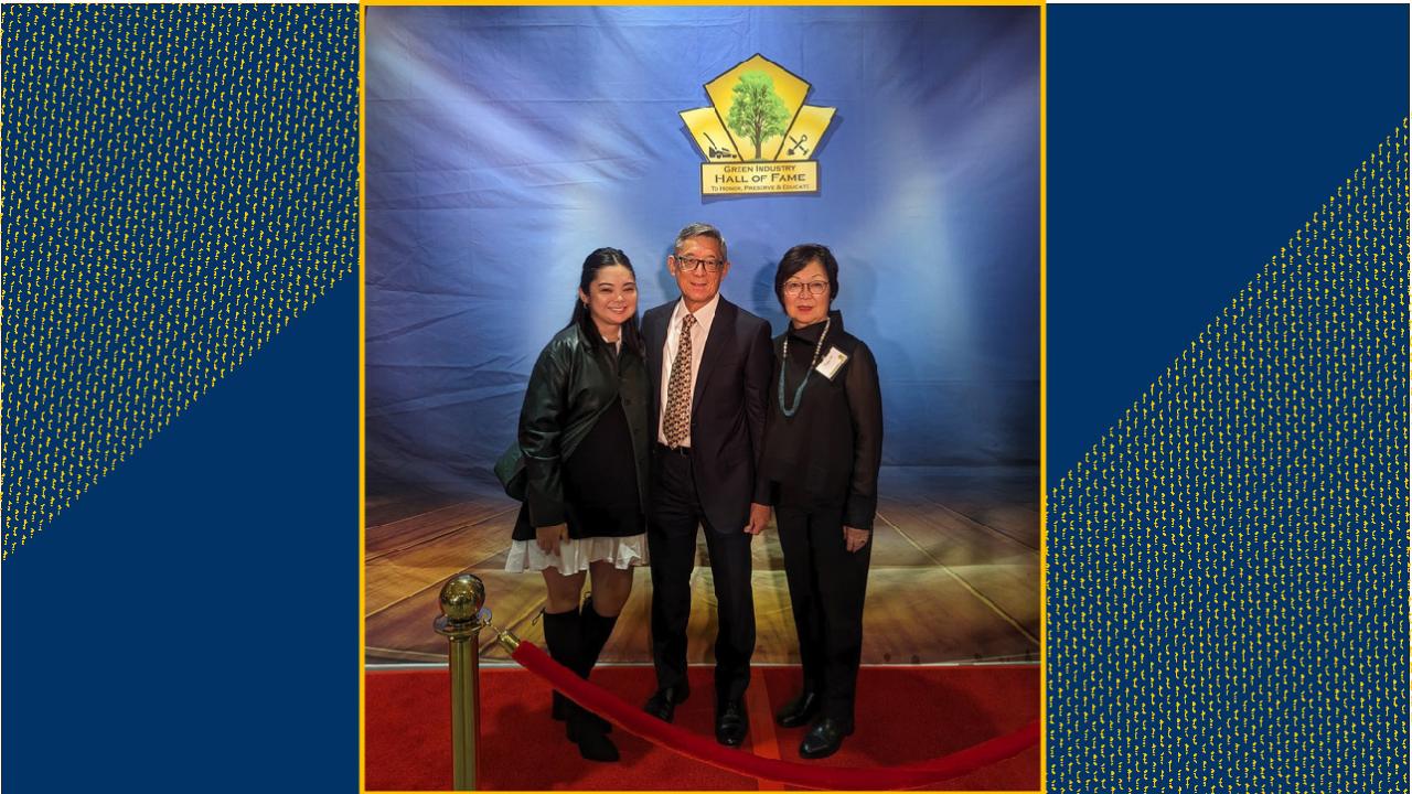 A husband, wife and their grown daughter on a stage, standing on a red carpet. Above them, a gold sign reads "Green Industry Hall of Fame."