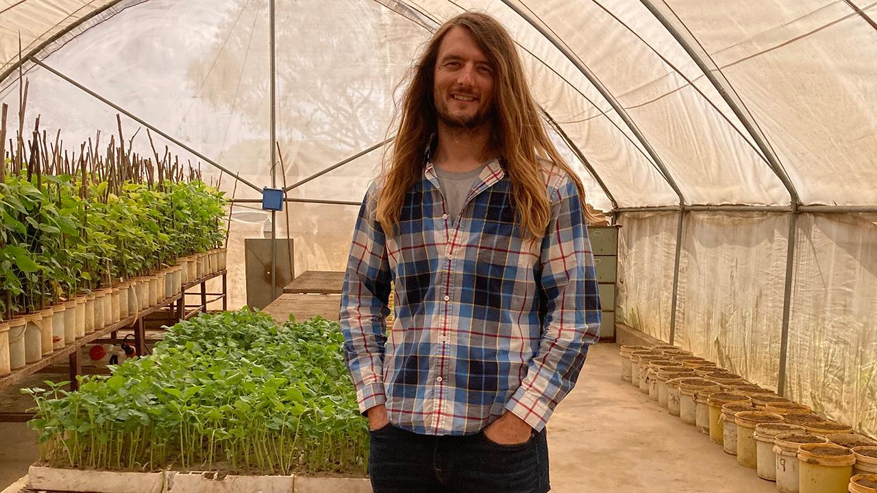 Man in a greenhouse with small, green plants.