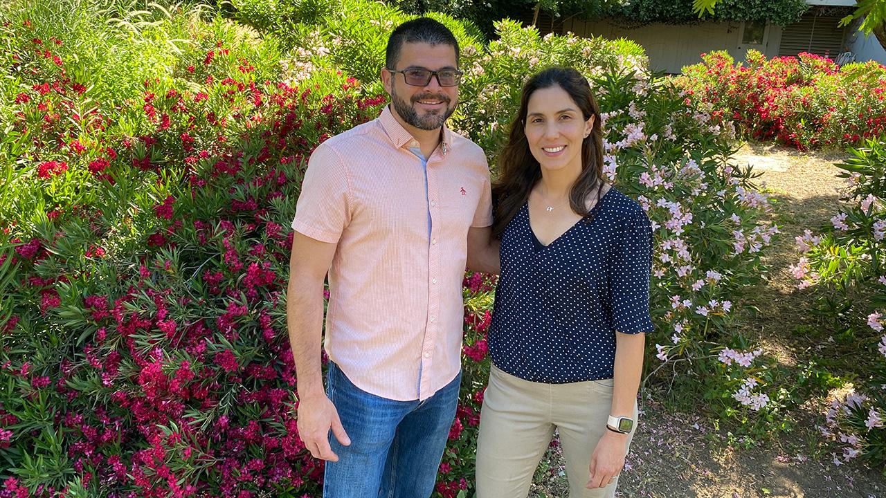 A man and a woman standing in a garden-like area with flowering plants.