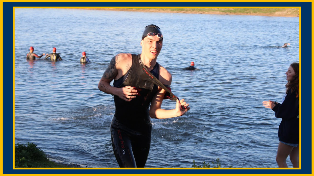Athlete in black wetsuit running from lake with swimmers behind him. UC Davis Department of Plant Sciences