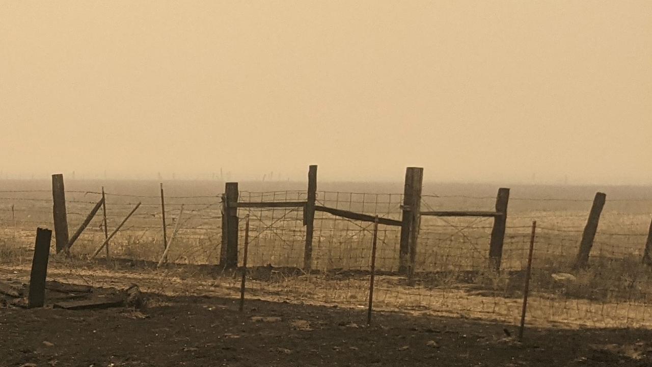 In a broad empty field, charred and broken fencing. The sky is grayish-orange. It looks like Armageddon.