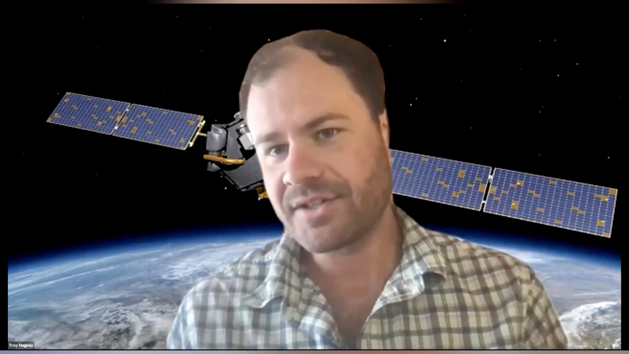 Troy Magney, seen from chest up, talks over Zoom. His background image is of a satellite orbiting Earth.