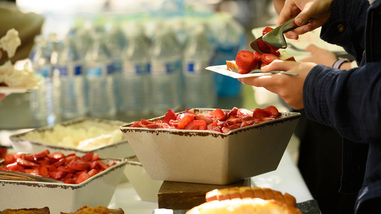 Two bowls of sliced strawberries and a plate of strawberries being held by someone