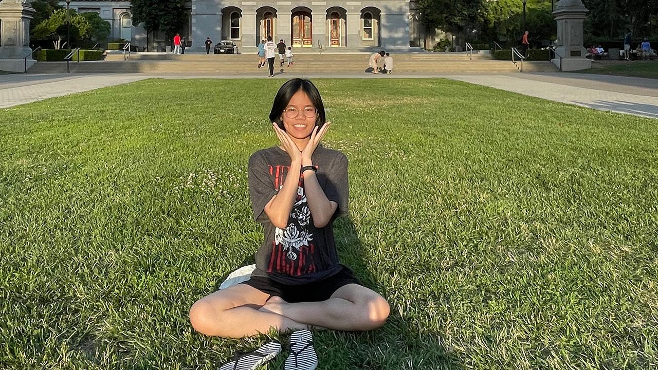 Young woman sitting cross-leged on green grass in front of U.S. Capitol