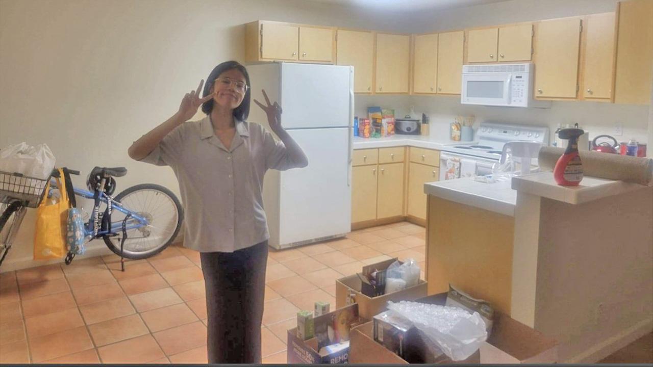 Young woman wearing a white shirt and black pants in nearly empty apartment