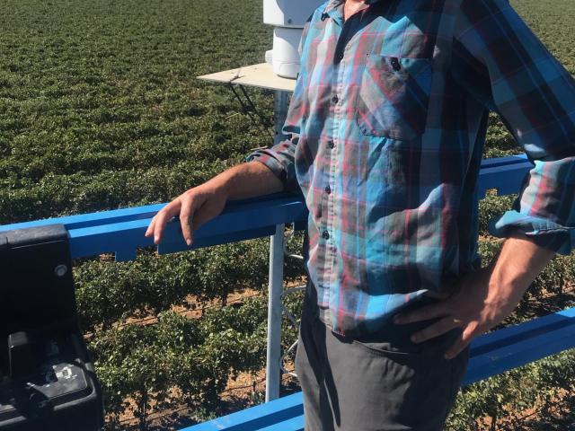 Magney poses before a scanning spectrometer with a vineyard as the background.