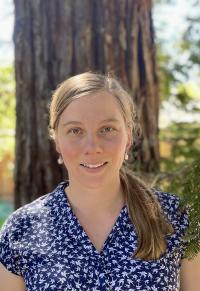 A young woman, Kimberly Gibson, faces the camera, standing before a redwood 