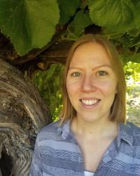 A young woman, Amy Groh, stands under a grapevine smiling