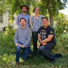 Three men and a woman stand in a tree-filled courtyard