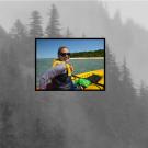 Woman in an orange kayak. Image placed over a cloud-shrouded forest