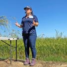 A woman in front of a rice field, next to a table, speaking