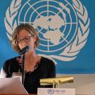 Woman speaking at a podium with the United Nations symbol behind  yher