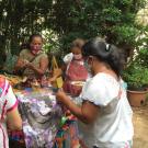 Women wearing traditional embroidered blouses are gathered around an outdoor cooking hearth.