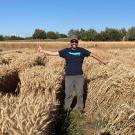 A man wearing a hat, standing in a field of light brown grass.