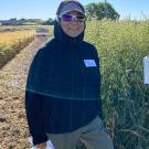 Woman bundled in wind-protective gear and sunglasses, standing by tall golden grain.