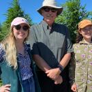 Two women and a man standing in front of cannabis plants in a field