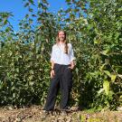 Young woman standing amid tall leafy green trees on a sunny day