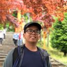 Asian man smiles in front of tree with red leaves 
