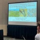 Young man talking at podium with projected slide and seated audience members. UC Davis Department of Plant Sciences