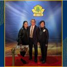 A husband, wife and their grown daughter on a stage, standing on a red carpet. Above them, a gold sign reads "Green Industry Hall of Fame."