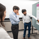 A younger man points to an academic poster, while an older man  looks on