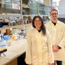 A woman and a man, wearing white lab coats and standing in a lab