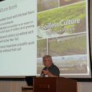 A man speaking, with a projector screen above him showing the words: “Soilless Culture book.”