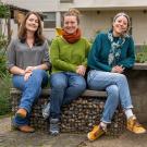 Three women sitting on a bench in a garden. They look happy