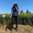 A woman standing in front of a field of grain, with blue sky above